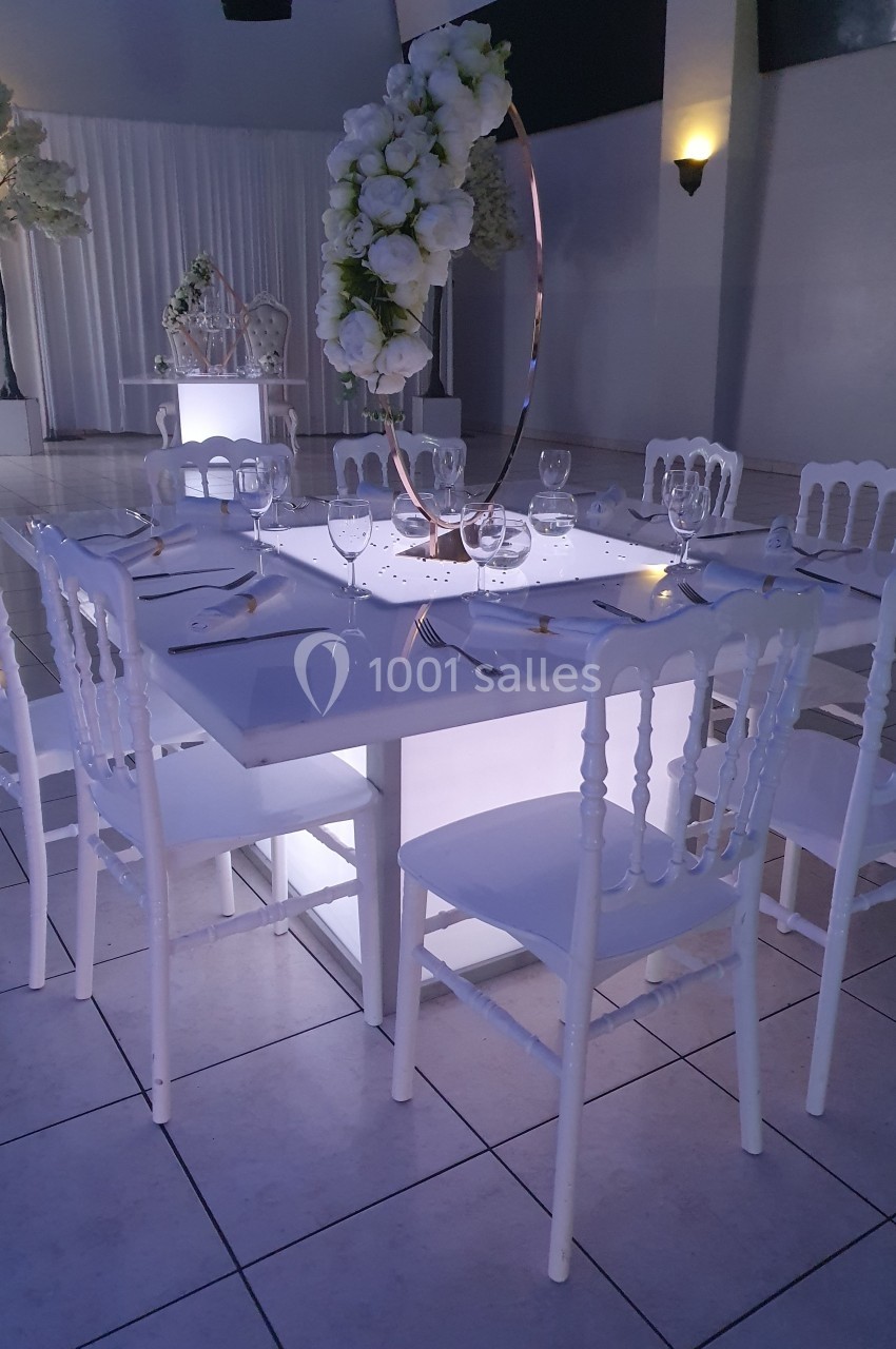 Location salle Crosne (Essonne) - Aux Tulipes #1 Table élégamment dressée avec des chaises blanches, centre de table floral et éclairage tamisé dans une salle de réception.