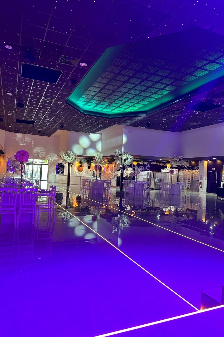 Location salle Crosne (Essonne) - Aux Tulipes #3 Salle de réception moderne avec éclairage violet, plafond étoilé et tables décorées de fleurs blanches.