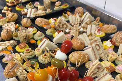 Plateaux garnis de divers amuse-bouches, sandwichs, brochettes et bouchées apéritives disposés sur une table.