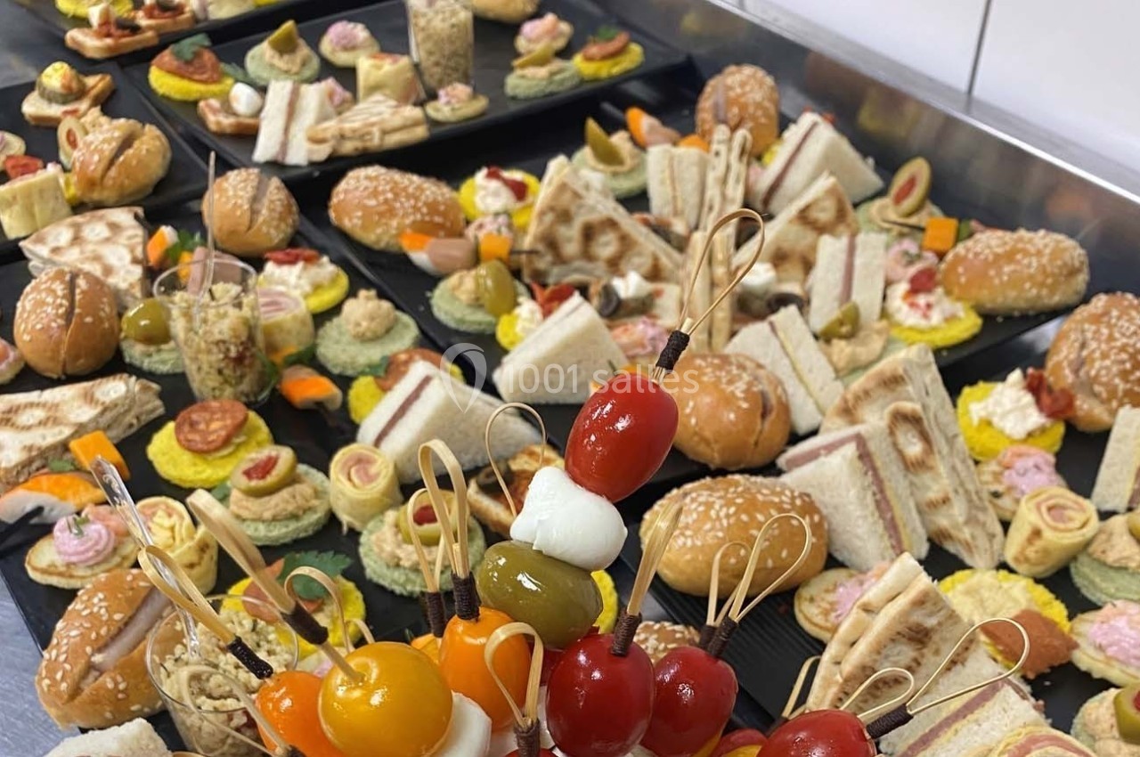 Plateaux garnis de divers amuse-bouches, sandwichs, brochettes et bouchées apéritives disposés sur une table.
