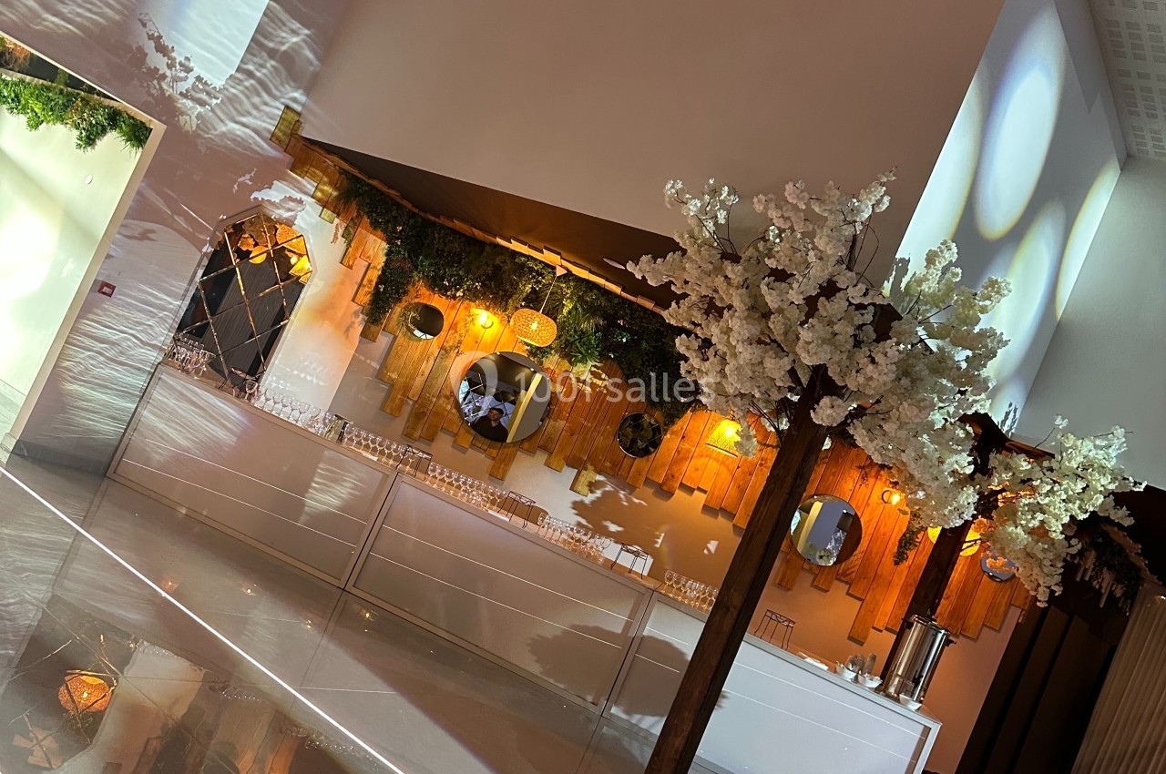 Décoration intérieure avec comptoir en bois, miroirs, guirlandes lumineuses et arbres artificiels ornés de fleurs blanches.