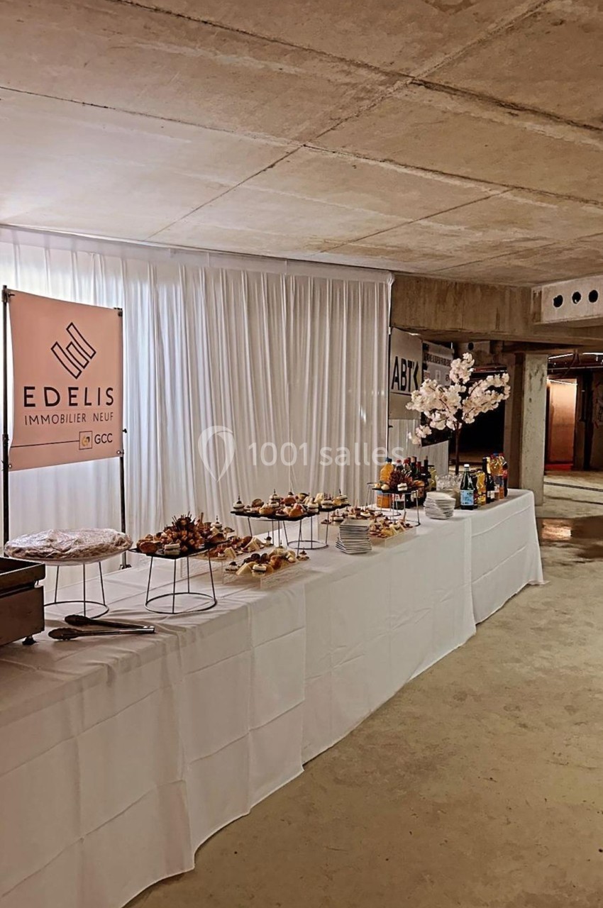 Table dressée avec des amuse-bouches et boissons dans un espace intérieur brut, décorée d'une bannière et d'un arbre fleuri.