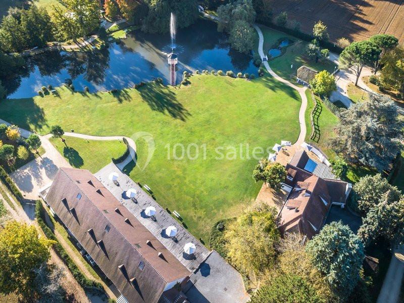 Vue aérienne d'un domaine avec un grand espace vert, un étang, une fontaine et plusieurs bâtiments entourés d'arbres.