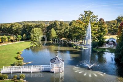 Pont éclairé et kiosque en bois près d'une fontaine illuminée, entourés d'arbres dans un parc nocturne.