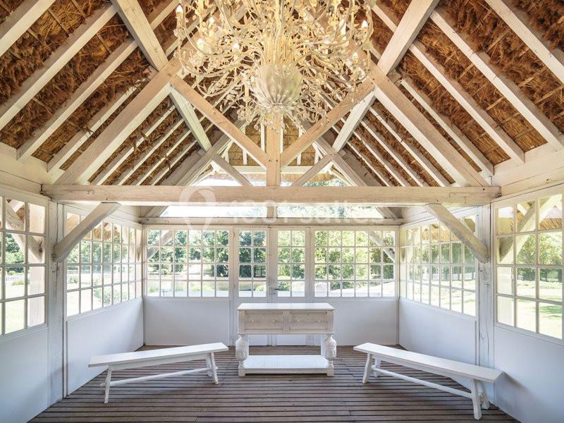 Intérieur lumineux d'une petite chapelle en bois avec des bancs blancs, un autel et un lustre décoratif.