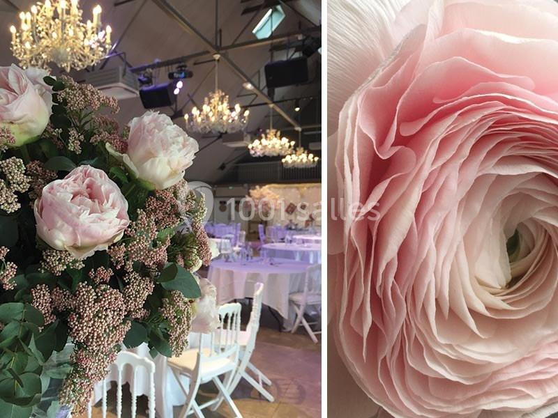 Décoration florale avec roses et feuillages dans une salle de réception éclairée par des lustres.