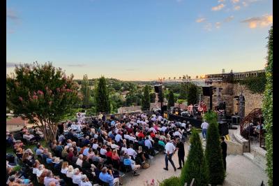 Miniature Location salle Montéléger (Drôme) - Orangerie du Château de Montéléger #8 Un concert en plein air au coucher du soleil, avec un public assis devant une scène entourée de verdure.