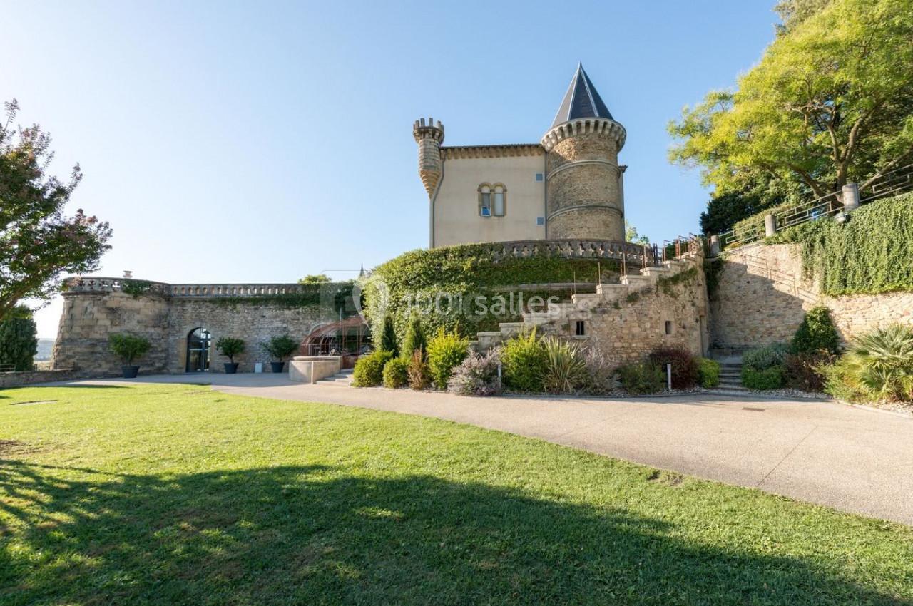 Château en pierre avec une tour ronde, entouré de végétation et d'une pelouse bien entretenue.