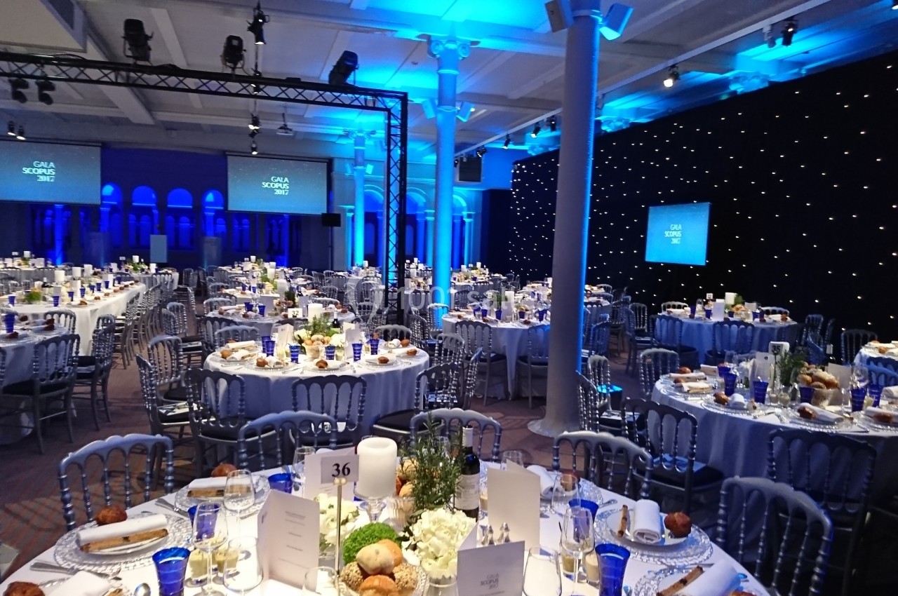 Salle de réception décorée pour un événement, avec tables dressées, éclairage bleu et écrans en arrière-plan.