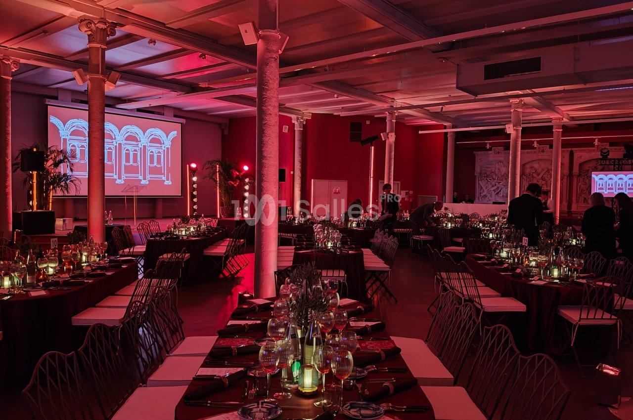 Salle de réception décorée avec des tables dressées, éclairage rouge tamisé et écrans projetant des images architecturales.