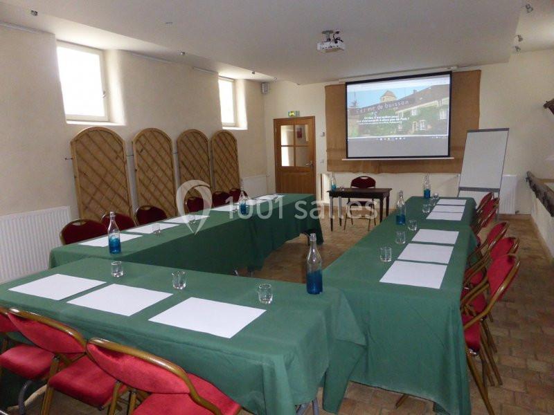 Salle de réunion avec tables en U couvertes de nappes vertes, chaises rouges, écran de projection et tableau blanc.