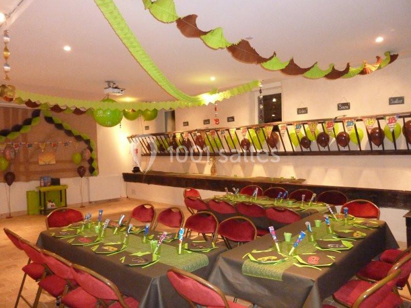 Salle décorée pour une fête avec des guirlandes vertes et marron, des ballons et des tables dressées.