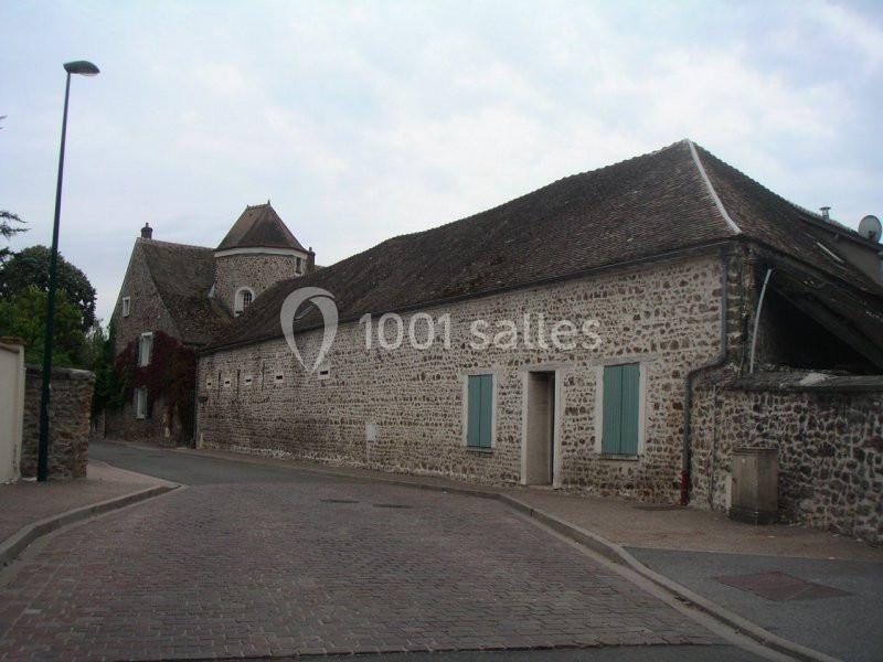Bâtiments en pierre avec volets bleus et toit en tuiles, bordant une rue pavée sous un ciel nuageux.
