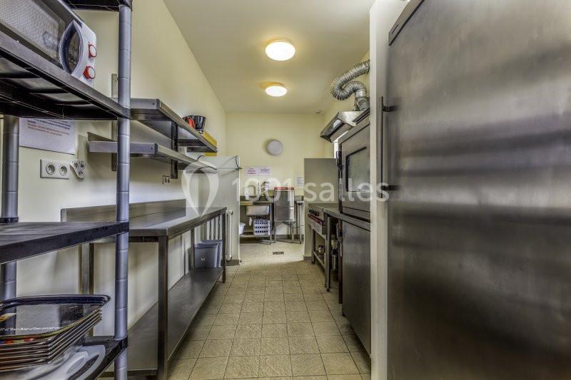 Cuisine professionnelle avec équipements en inox, étagères de rangement, four et éclairage au plafond.