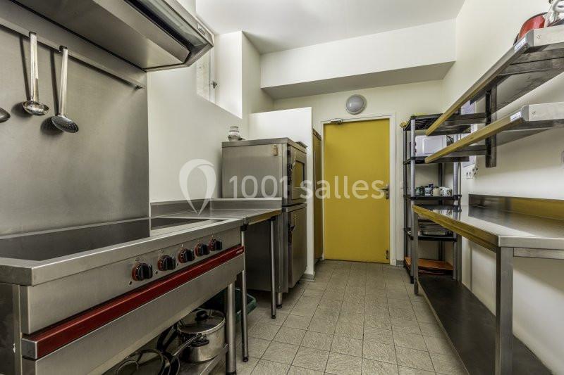 Cuisine professionnelle avec équipements en inox, étagères de rangement, four et porte jaune au fond.
