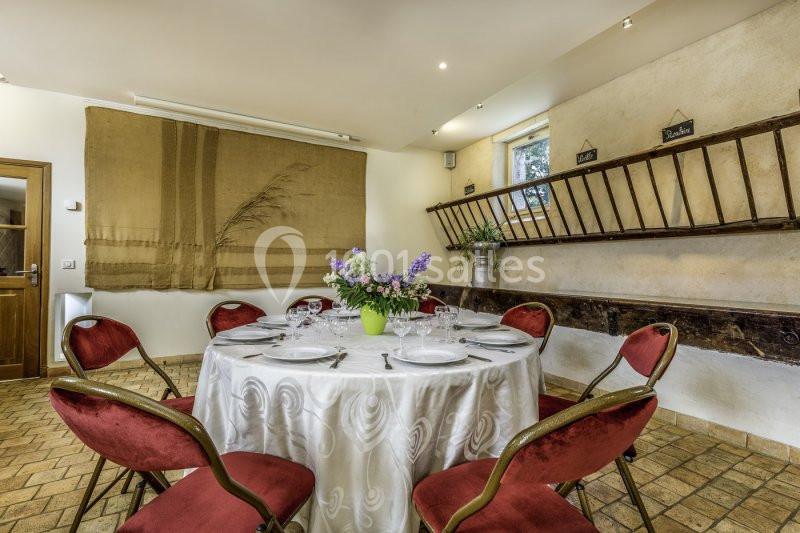 Table ronde dressée avec une nappe blanche, entourée de chaises rouges, dans une salle rustique avec décoration murale.