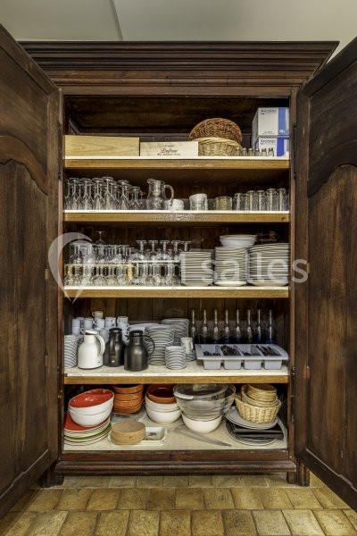 Armoire en bois ouverte contenant des verres, assiettes, bols, carafes et paniers soigneusement rangés sur des étagères.