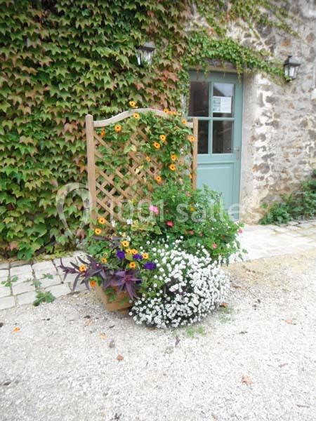 Treillis en bois orné de fleurs colorées devant un mur en pierre couvert de lierre et une porte verte.