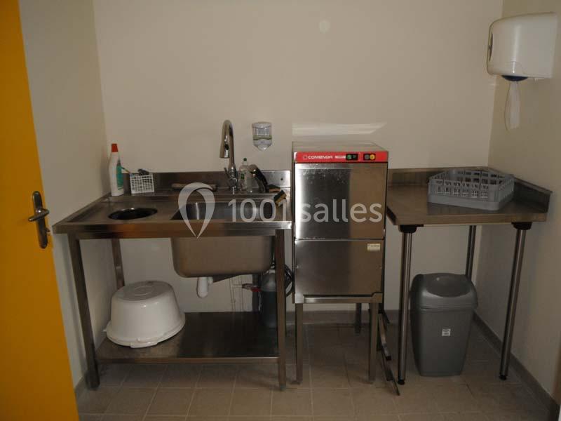 Évier en inox avec lave-vaisselle professionnel, étagères, poubelle et distributeur de papier dans une pièce utilitaire.