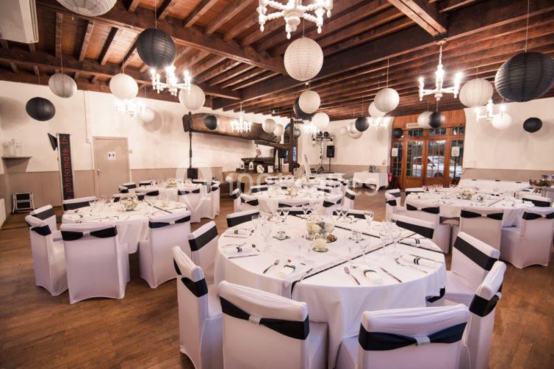 Salle de réception décorée avec des tables rondes dressées, des chaises blanches et des lanternes suspendues.