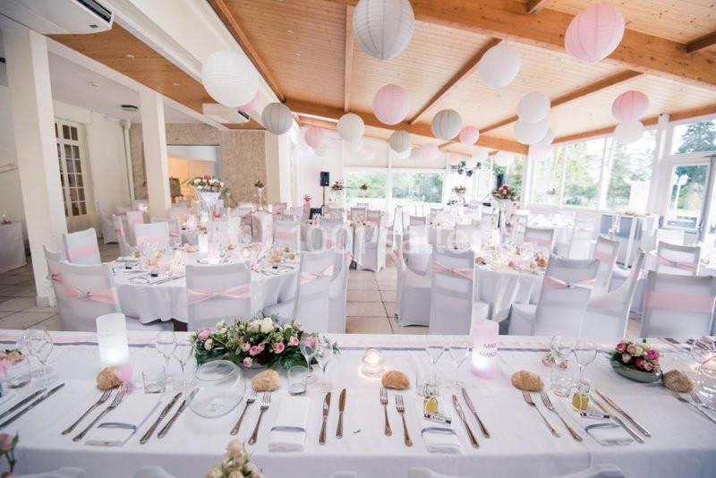Salle de réception décorée pour un mariage, avec tables dressées, nappes blanches et lanternes suspendues.