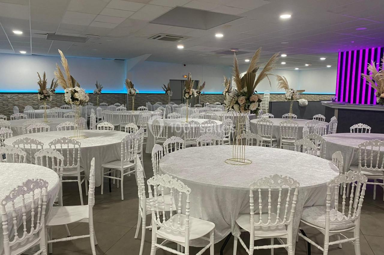 Salle de réception aménagée avec des tables rondes décorées de nappes blanches et des chaises blanches élégantes.