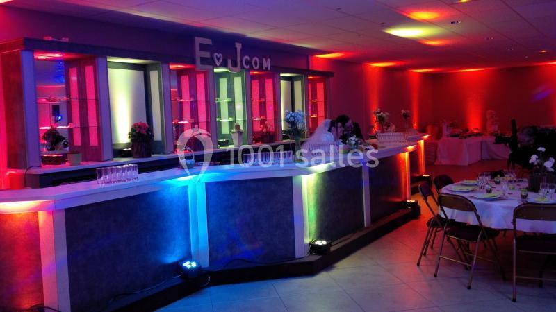 Bar lumineux avec éclairage coloré dans une salle de réception, tables dressées en arrière-plan.