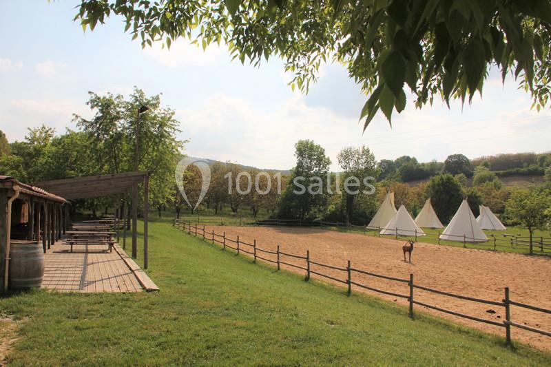 Un enclos avec un cheval, des tipis blancs en arrière-plan et une terrasse en bois bordée d'arbres.
