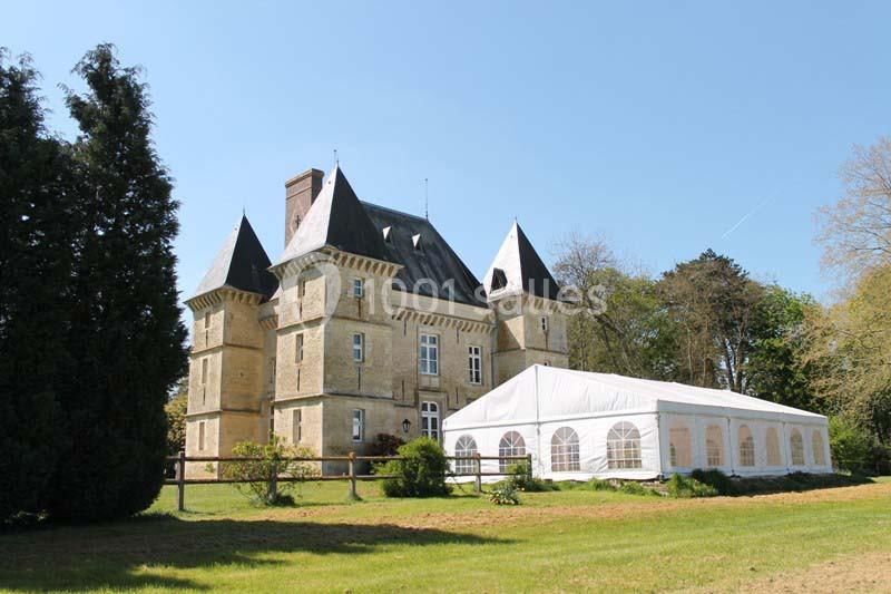 Château en pierre avec quatre tours, entouré de verdure, et une grande tente blanche installée sur la pelouse.