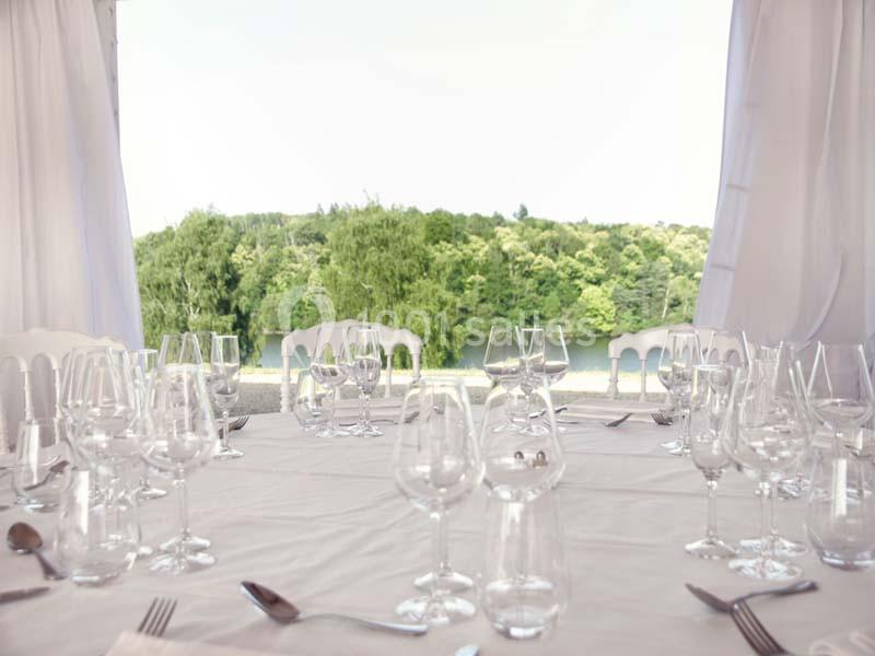 Location salle Meyrignac-l'Église (Corrèze) - Domaine des Monédières #5 Table dressée avec nappes blanches, verres et couverts, offrant une vue sur un paysage verdoyant et un plan d'eau.