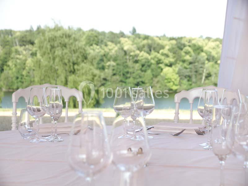 Location salle Meyrignac-l'Église (Corrèze) - Domaine des Monédières #9 Table dressée avec nappes blanches, verres et couverts, en extérieur avec vue sur un paysage verdoyant et une rivière.