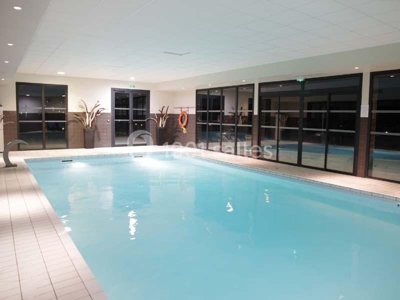 Location salle Meyrignac-l'Église (Corrèze) - Domaine des Monédières #17 Piscine intérieure éclairée avec carrelage clair, grandes baies vitrées et plantes décoratives.