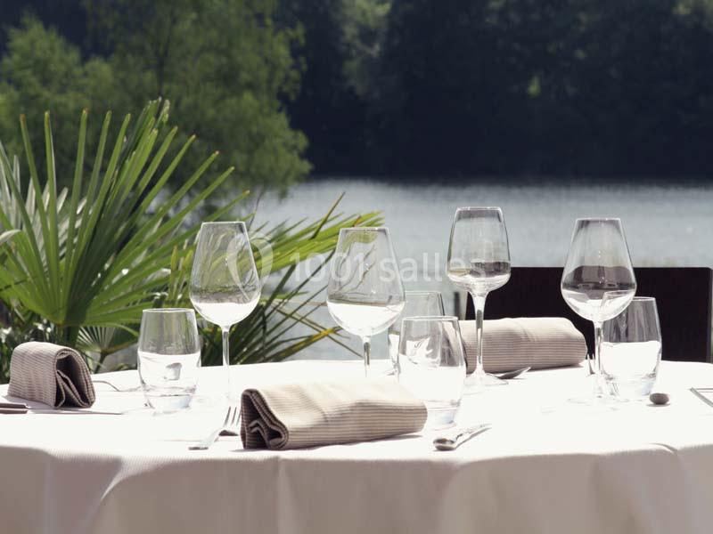 Location salle Meyrignac-l'Église (Corrèze) - Domaine des Monédières #21 Table dressée avec des verres et serviettes en tissu, en extérieur avec vue sur un lac et des arbres en arrière-plan.