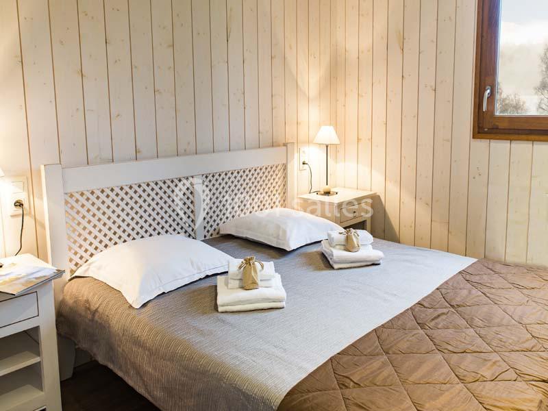 Location salle Meyrignac-l'Église (Corrèze) - Domaine des Monédières #20 Chambre lumineuse avec lit double, draps blancs, plaid marron, tables de chevet et mur en bois clair.