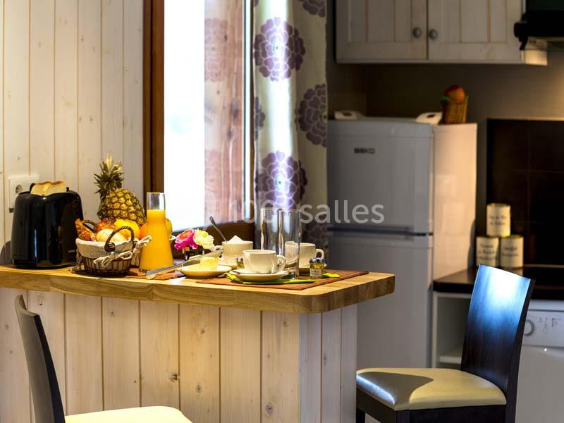 Location salle Meyrignac-l'Église (Corrèze) - Domaine des Monédières #22 Petit-déjeuner servi sur un comptoir en bois dans une cuisine lumineuse avec réfrigérateur et décoration florale.