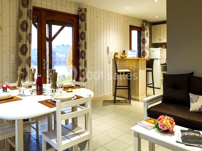 Location salle Meyrignac-l'Église (Corrèze) - Domaine des Monédières #23 Salle à manger lumineuse avec table dressée, coin salon, cuisine ouverte et vue sur l'extérieur par une porte vitrée.