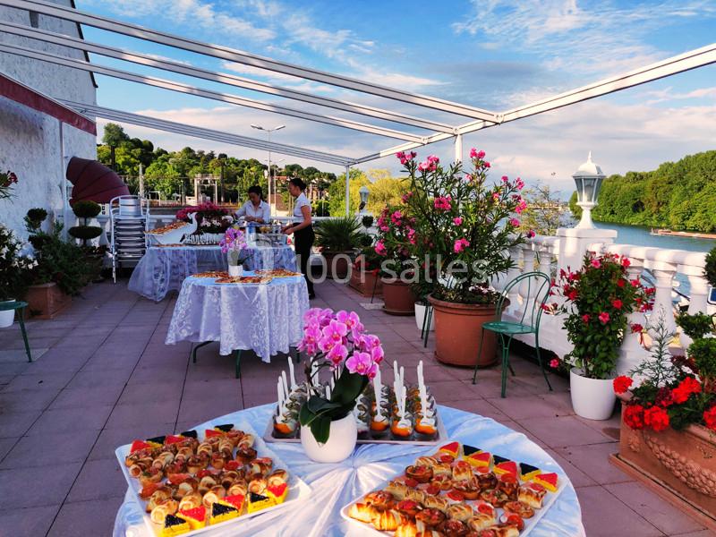 Terrasse aménagée avec des tables garnies de plats et décorée de fleurs, surplombant un paysage verdoyant.