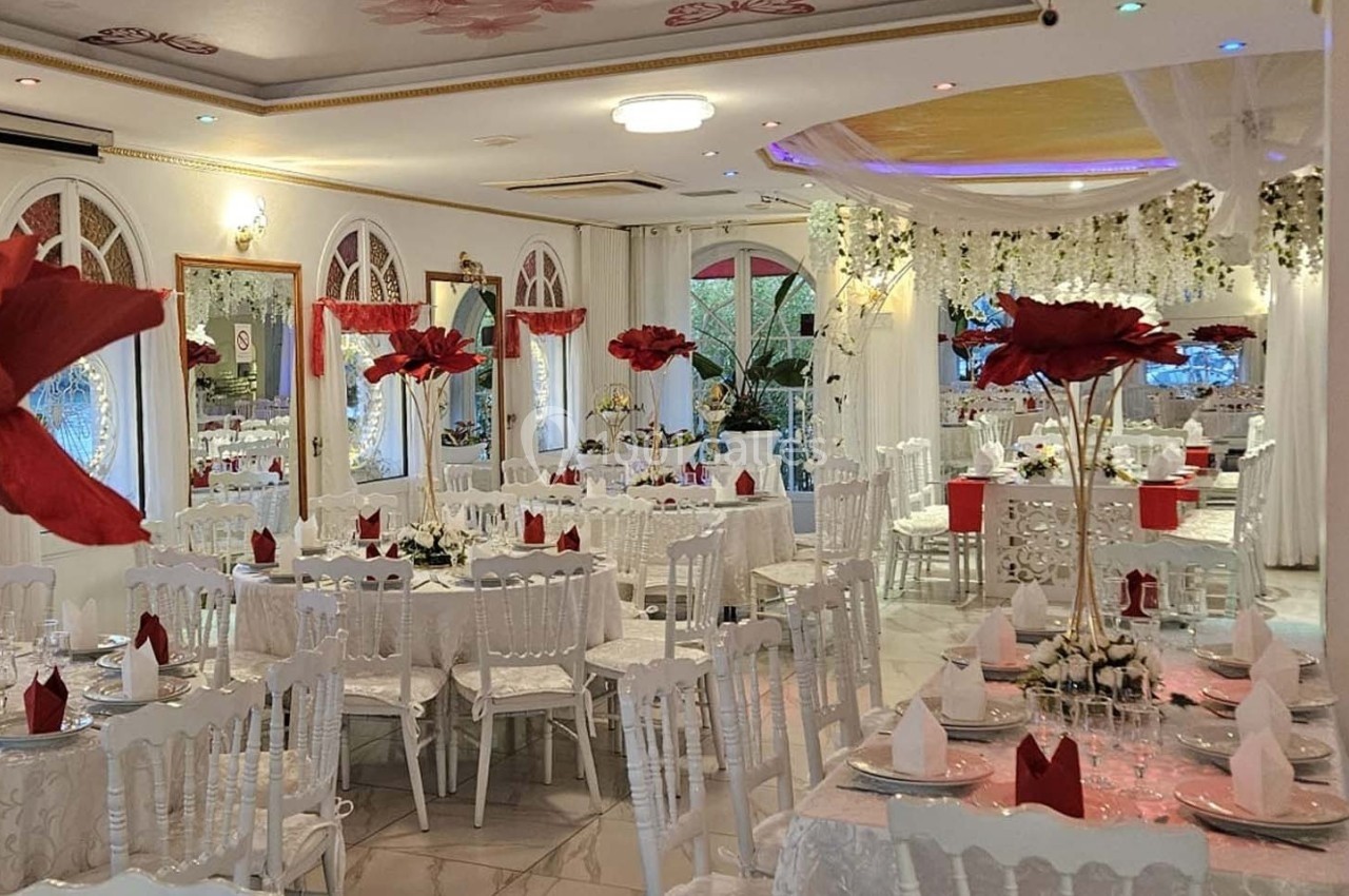 Salle de réception élégante décorée de blanc et de rouge, avec des tables dressées et des fleurs suspendues.