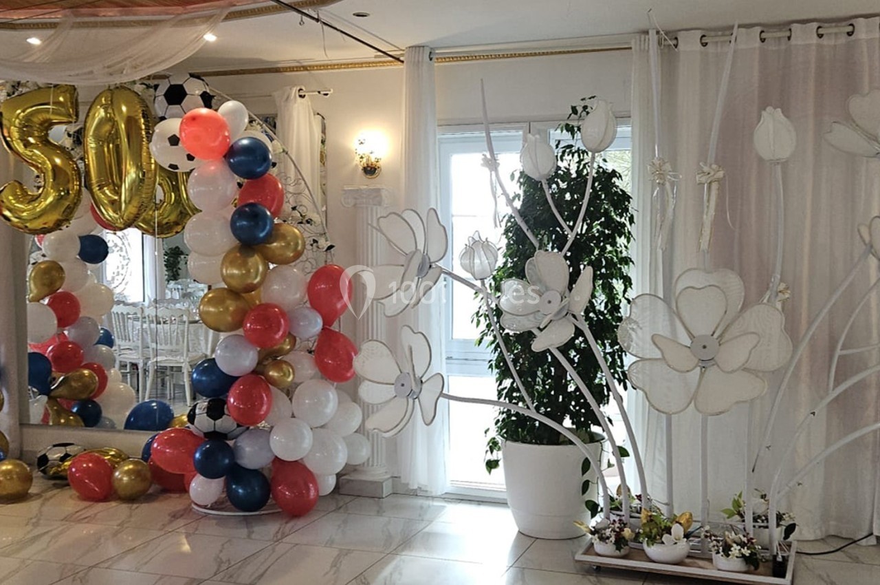 Décoration festive avec ballons colorés et chiffres dorés ’50’ dans une salle ornée de rideaux et plantes.