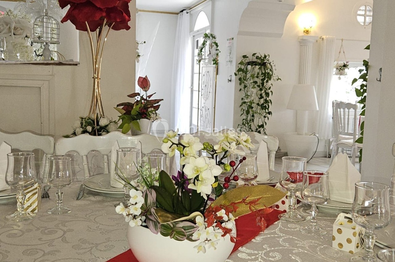 Table élégamment dressée avec nappe blanche, vaisselle raffinée et décoration florale dans une salle lumineuse.