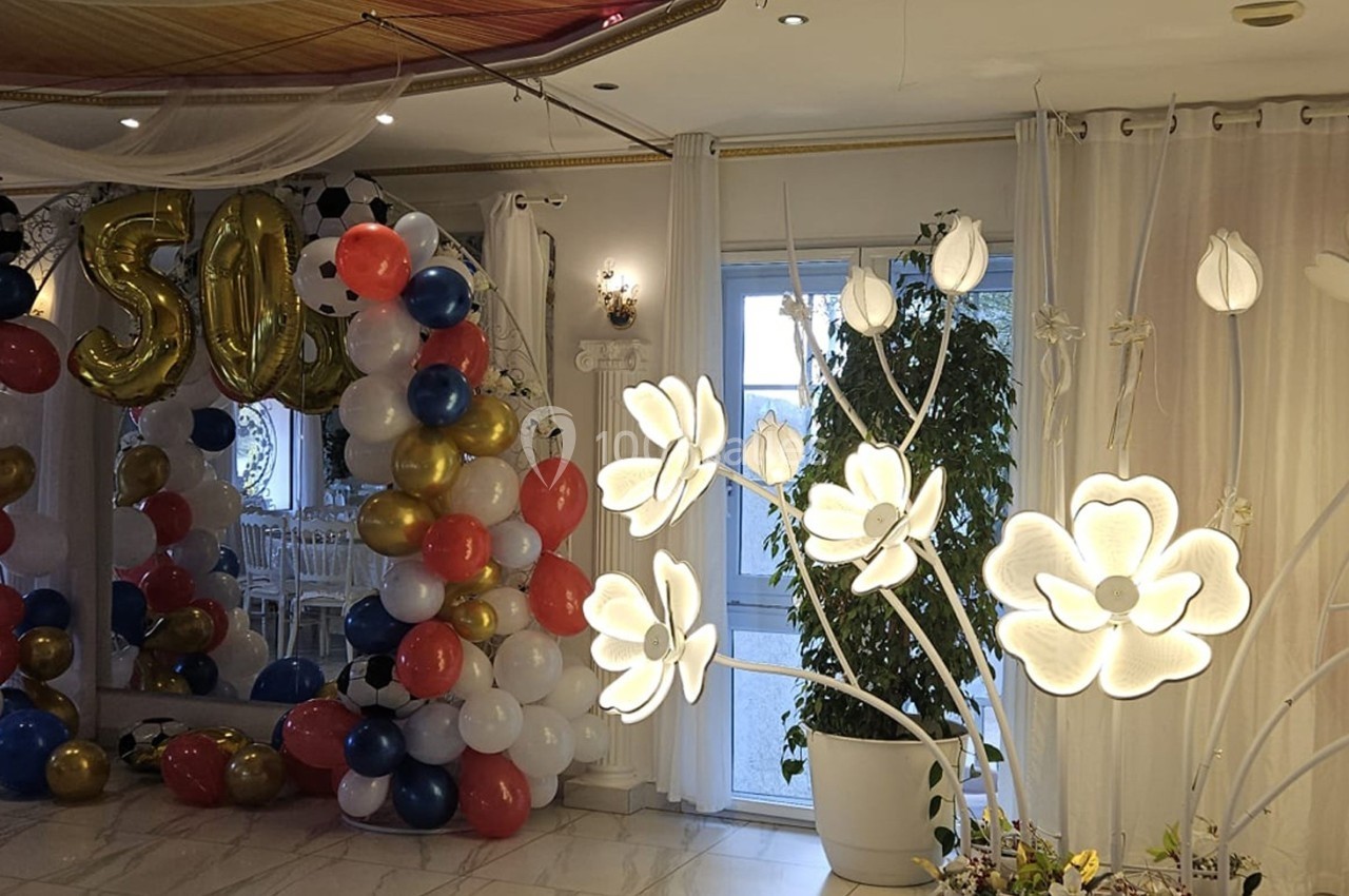 Décoration de salle avec arche de ballons colorés, chiffres ’50’ dorés et lampes en forme de fleurs lumineuses.