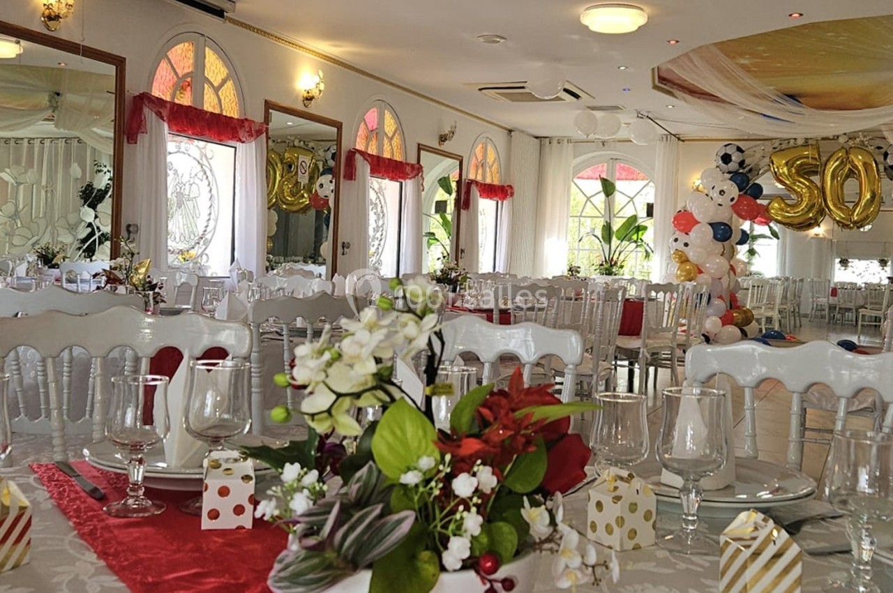 Salle de réception décorée avec des tables dressées, des ballons colorés et une arche marquée ’50’.
