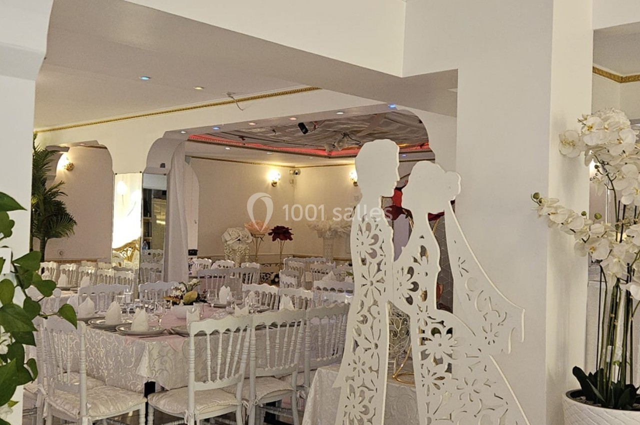 Salle de réception décorée avec des tables dressées, des chaises blanches et des ornements floraux blancs.