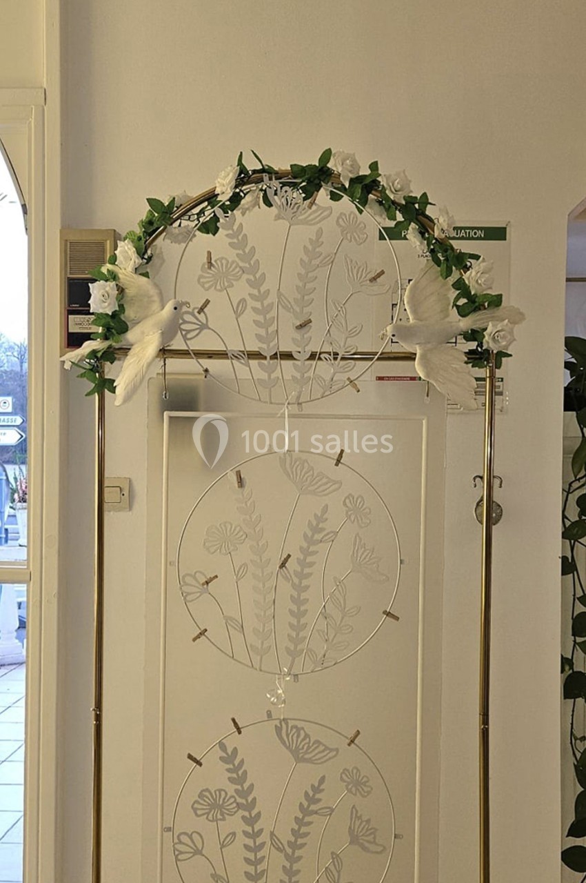 Arche décorative dorée ornée de fleurs blanches et de feuillage, placée devant un panneau floral blanc.