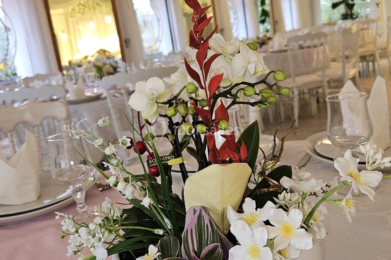 Centre de table floral avec des orchidées blanches et rouges, entouré de vaisselle sur une table de réception élégante.