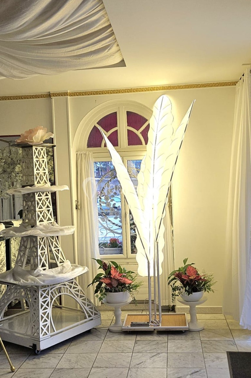 Lampadaire en forme de feuilles blanches éclairé, entouré de plantes et d'une décoration en forme de tour Eiffel blanche.