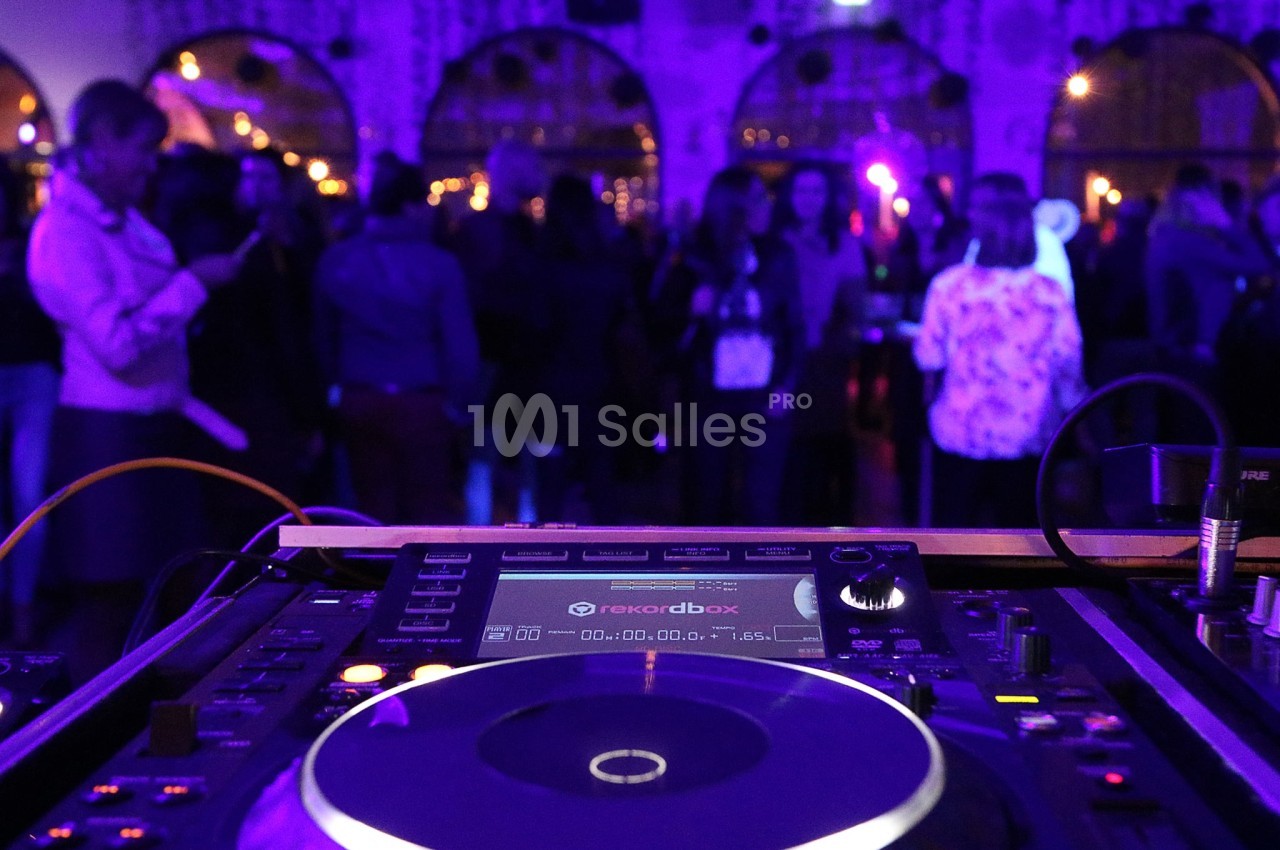 Platines de DJ en gros plan avec une foule dansante en arrière-plan sous des lumières tamisées.