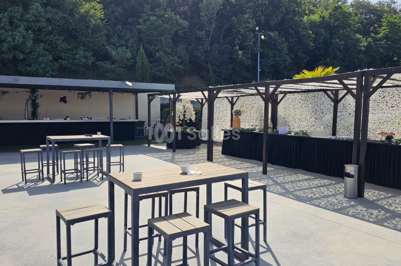 Terrasse extérieure avec tables et chaises en métal, pergolas ombragées et un comptoir en arrière-plan.