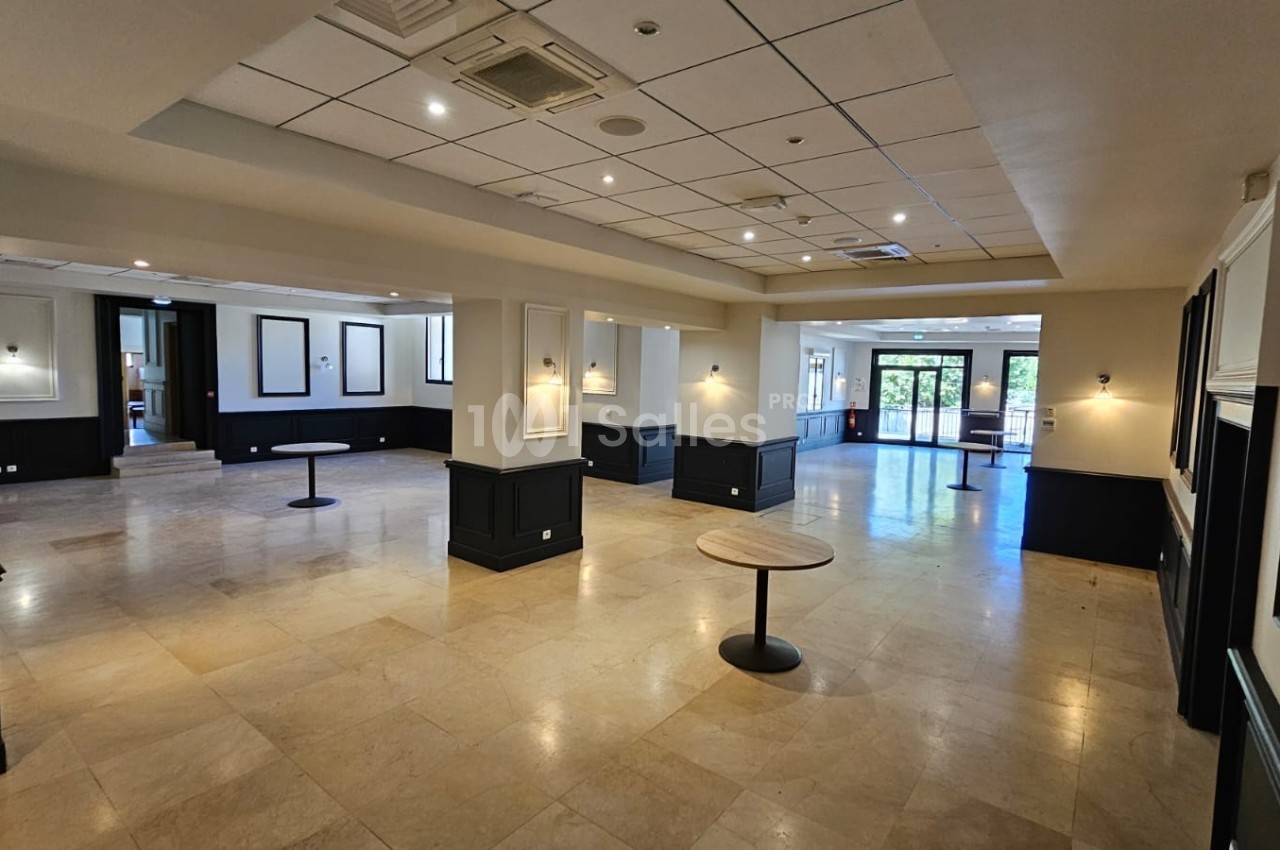 Salle spacieuse avec sol en marbre, murs clairs, éclairage encastré et quelques tables rondes dispersées.