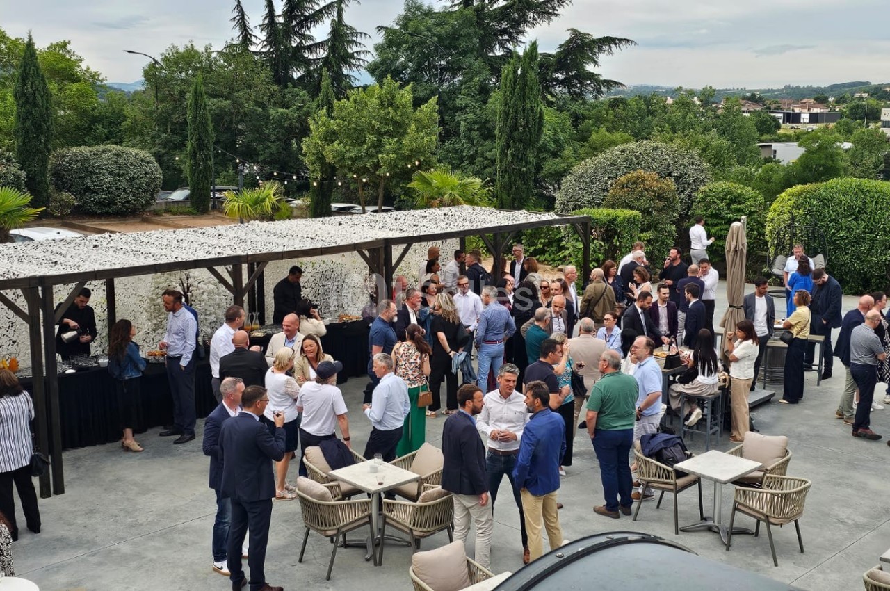 Groupe de personnes rassemblées en extérieur sur une terrasse, discutant autour de tables et d'un buffet.